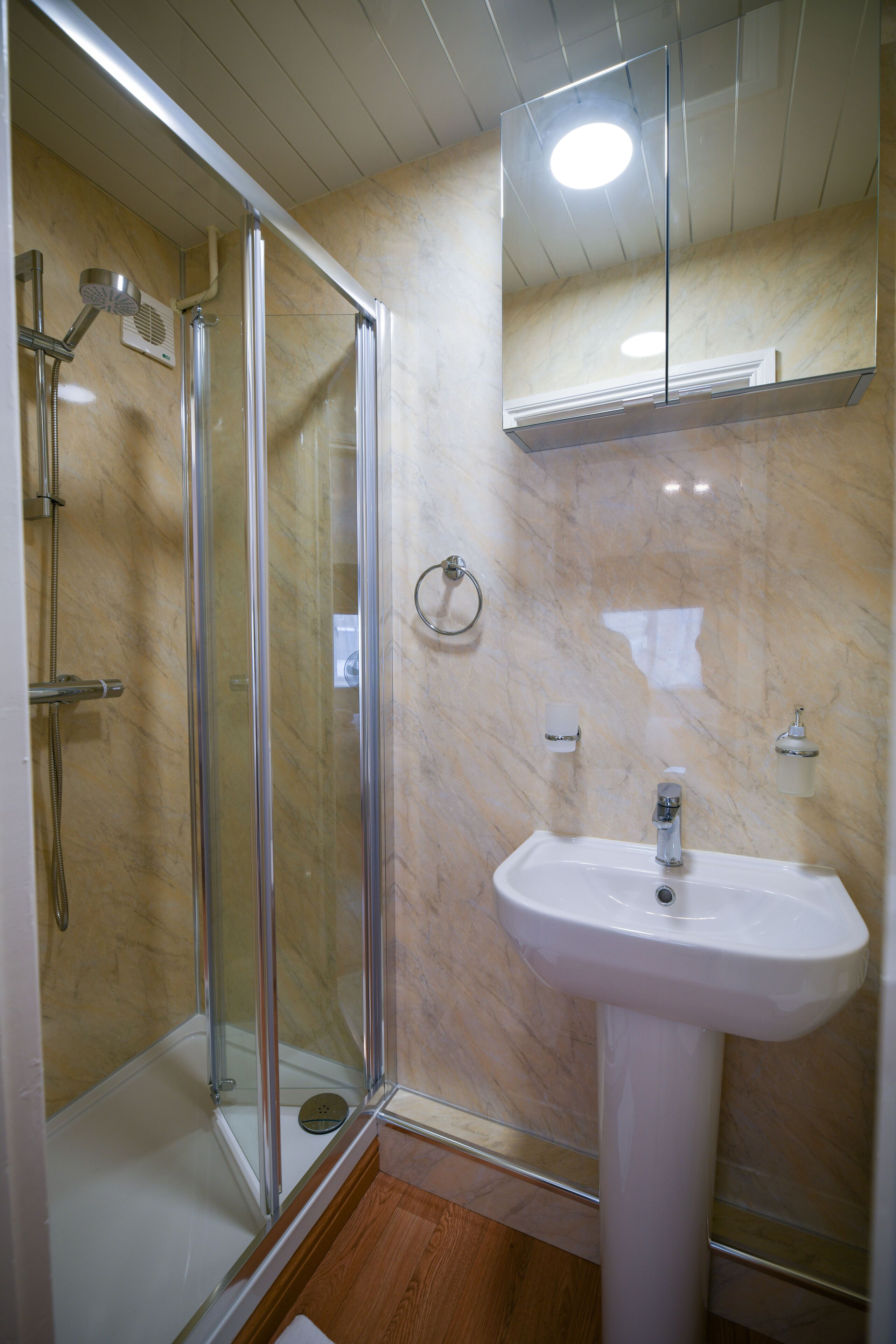 Une salle de bain dotée d’une douche à parois de verre, d’un lavabo sur pied blanc et de murs en marbre.