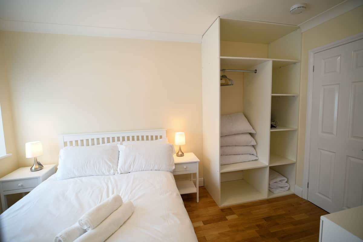A bedroom with a bed, nightstands, a lamp, an open closet with shelves, and a door.