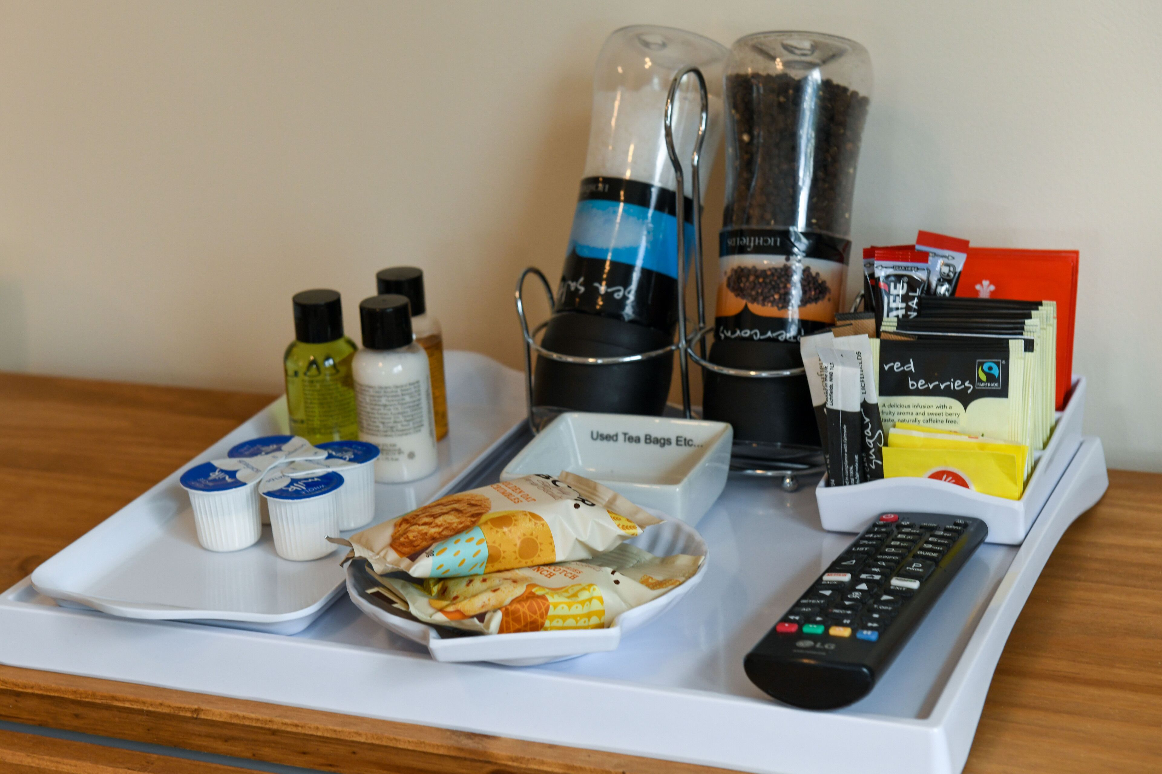 A tray with tea bags, a remote control, and a container of snacks.
