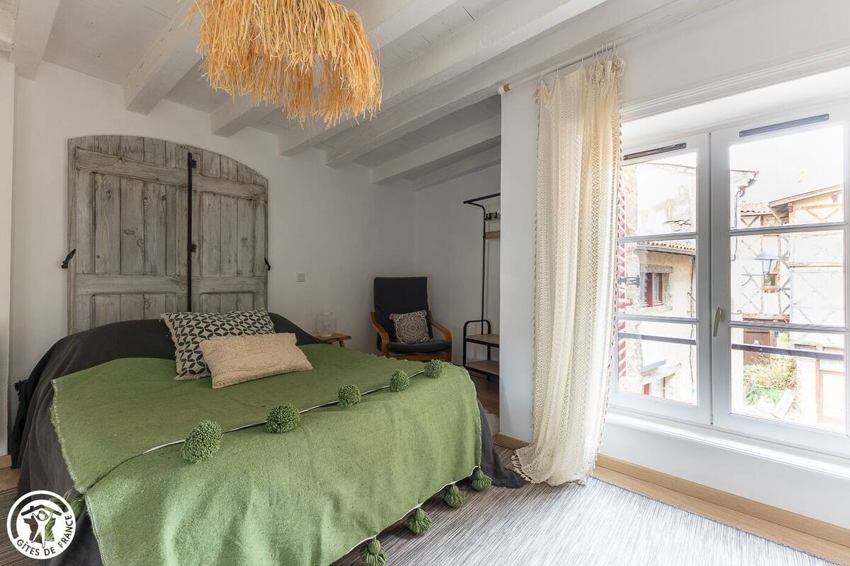 Quarto com cama, cadeira, janela com cortinas e porta de madeira rústica.