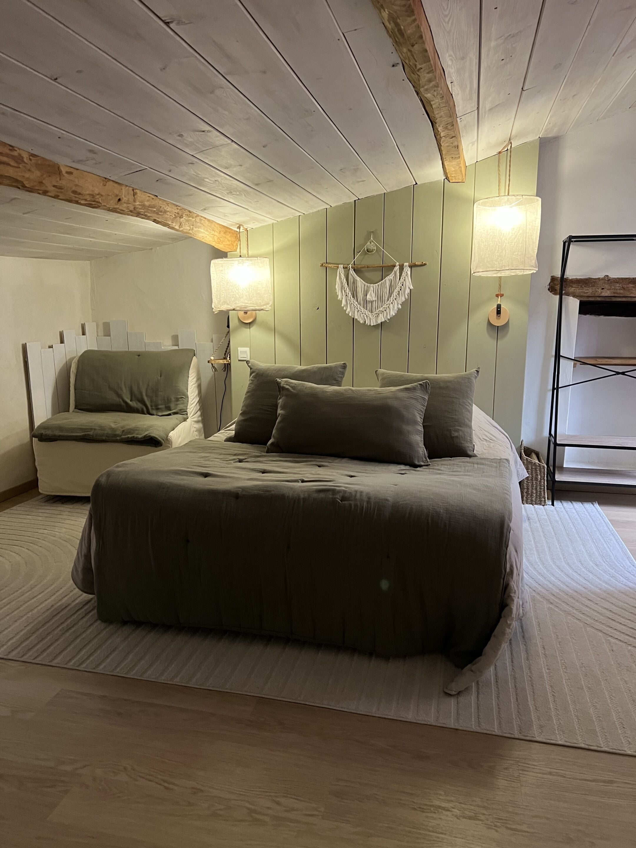 A bedroom with a bed, bedside lamps, a macrame wall hanging, and a wooden ladder.