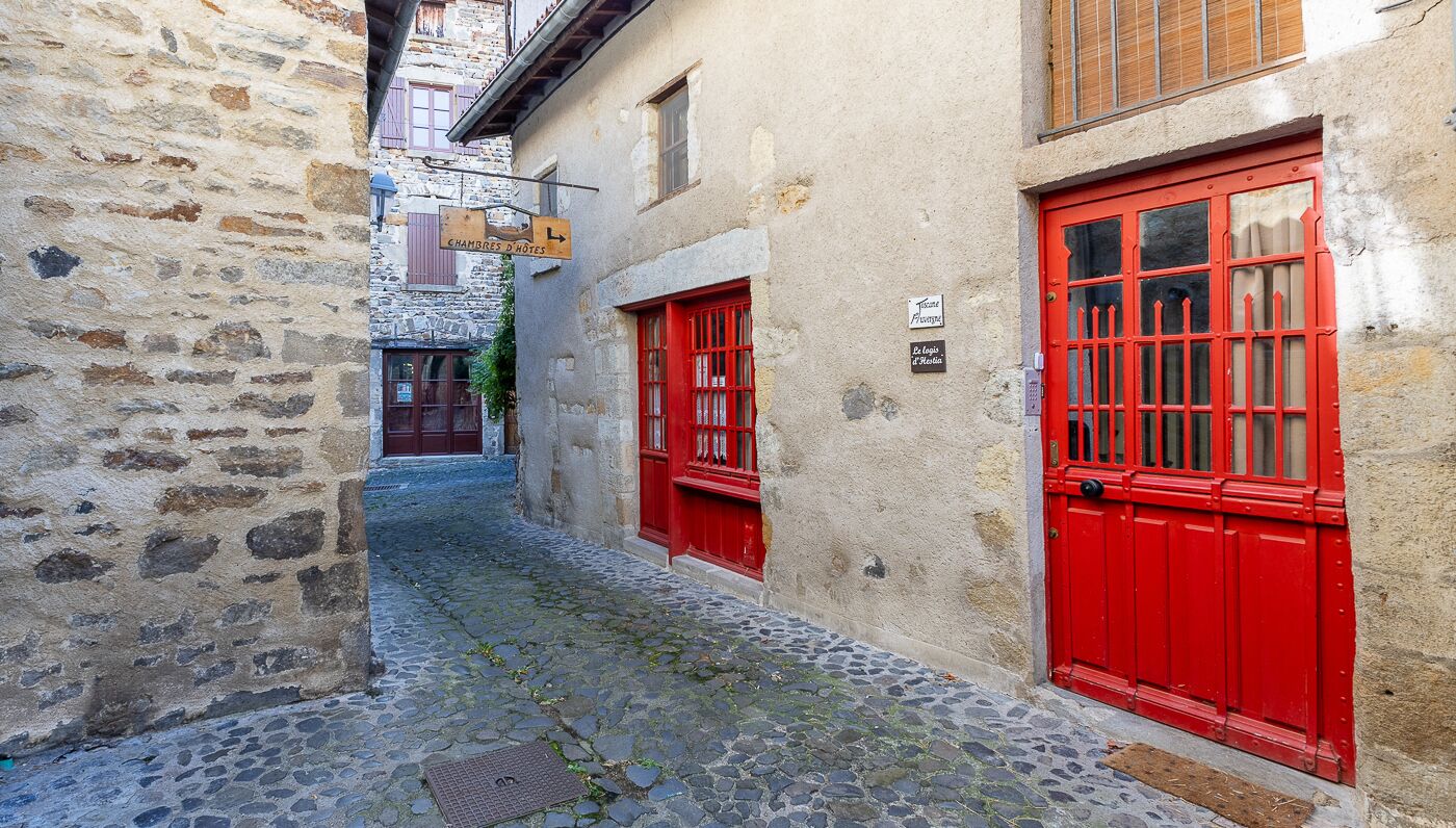 Une ruelle étroite pavée de pierres, avec des portes rouges et des murs en pierre.