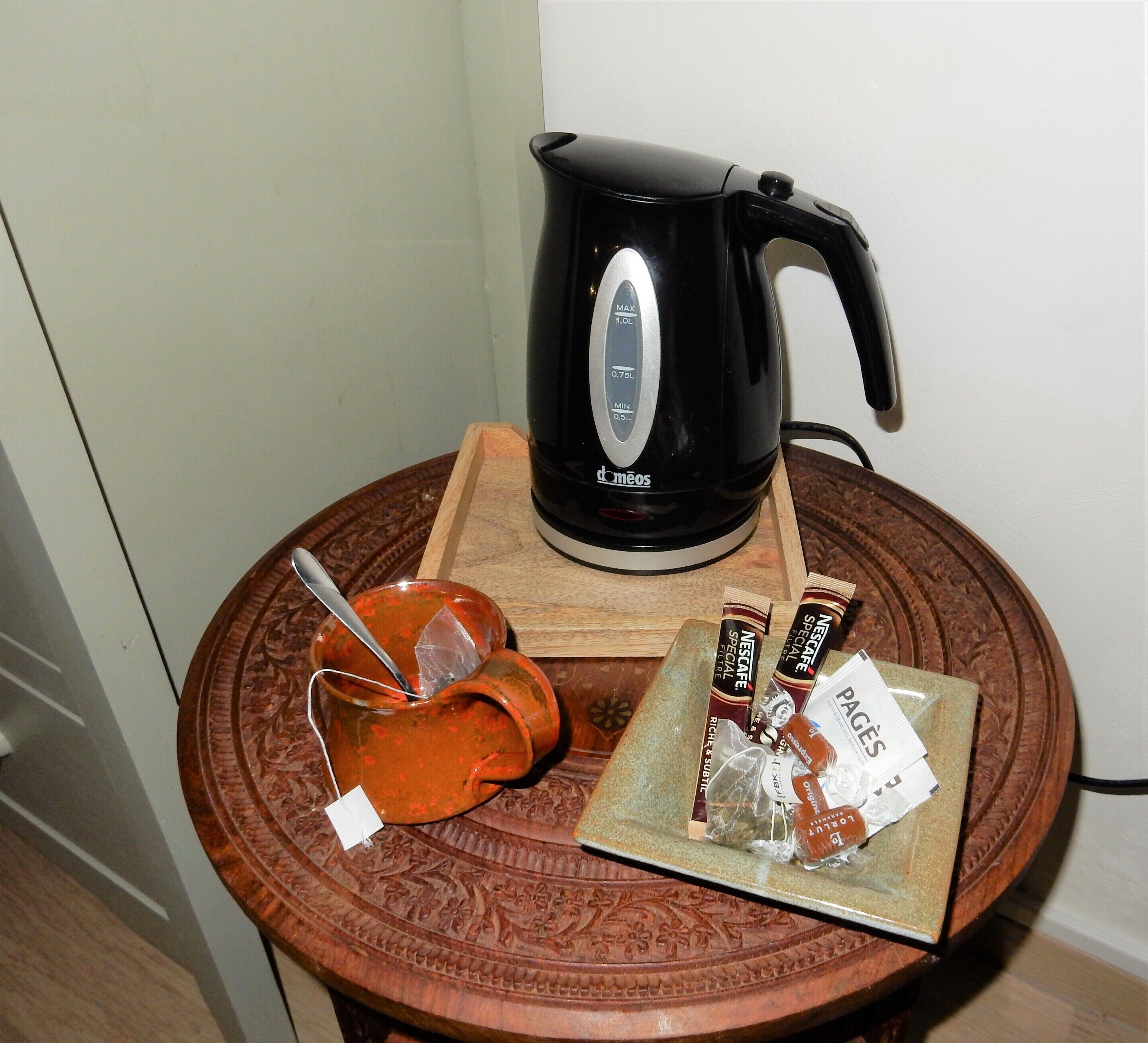 A coffee maker, a mug, and a tray with coffee pods on a round wooden table.