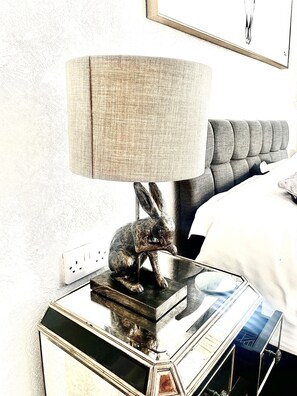 A lamp with a textured shade, a rabbit figurine, and a modern bedside table.