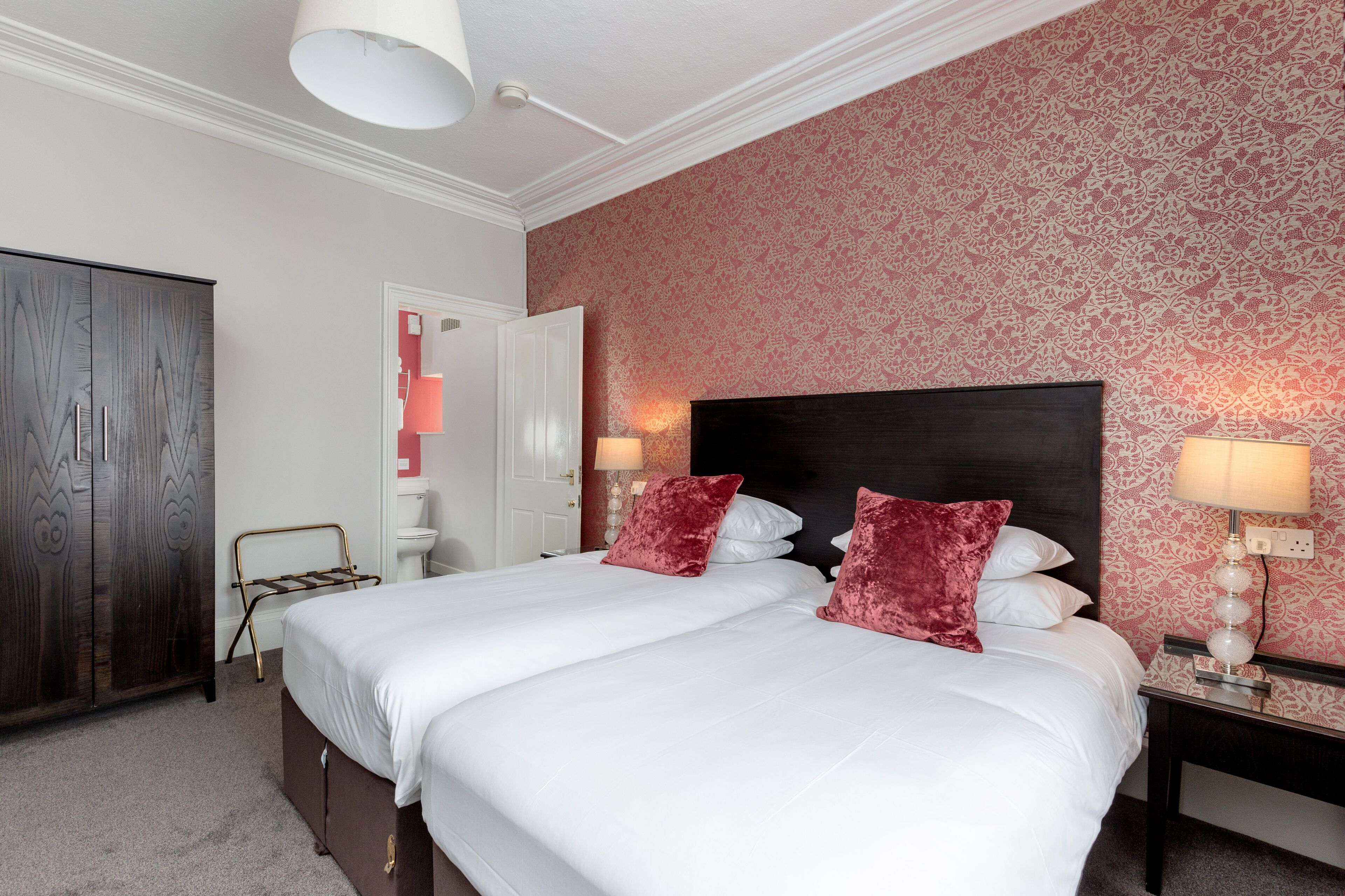 Een hotelkamer met een groot bed, twee nachtkastjes met lampen, een kledingkast en een zichtbare badkamer door een open deur.