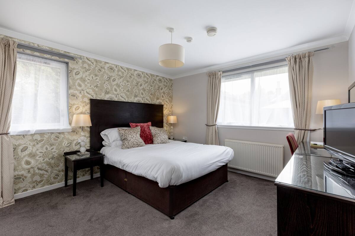 A bedroom with a large bed, a nightstand, a TV, and a desk.