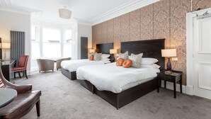 A hotel room with two beds, a sitting area with a table and chairs, and a large window providing a view. - The Kirkstyle Hotel (Biggar)