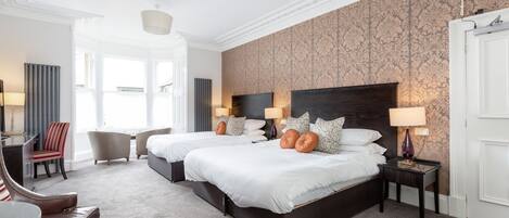 A hotel room with two beds, a sitting area with a table and chairs, and a large window providing a view.