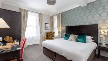A hotel room with a large bed, a desk, a chair, and a window with curtains.
