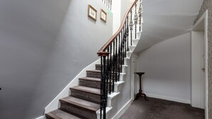 A staircase with a wooden handrail and black balusters, carpeted steps, and a white wall with two framed pictures. - The Kirkstyle Hotel (Biggar)