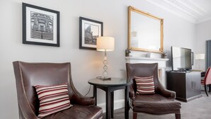 A room with two leather armchairs, a round table with a lamp, framed pictures on the wall, a large mirror, and a fireplace. - The Kirkstyle Hotel (Biggar)