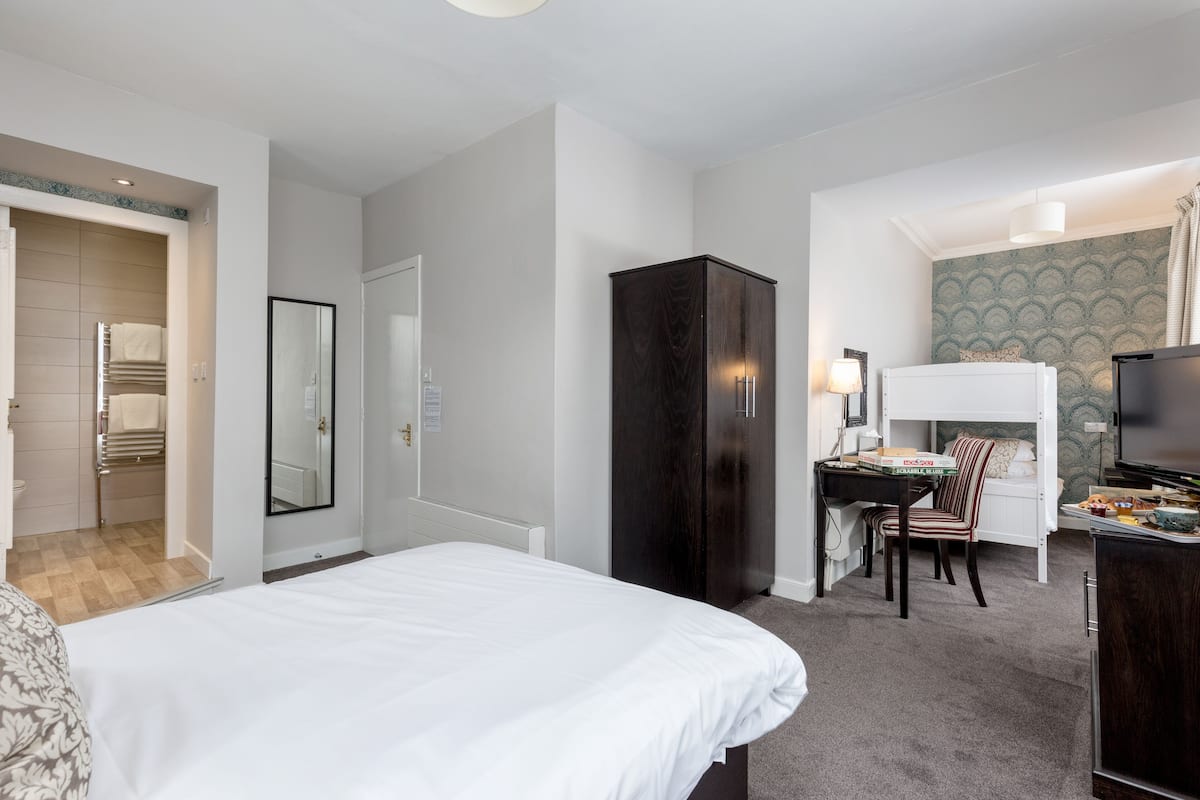 A hotel room with a bed, a desk with a chair, a wardrobe, a television, and a small kitchenette area.