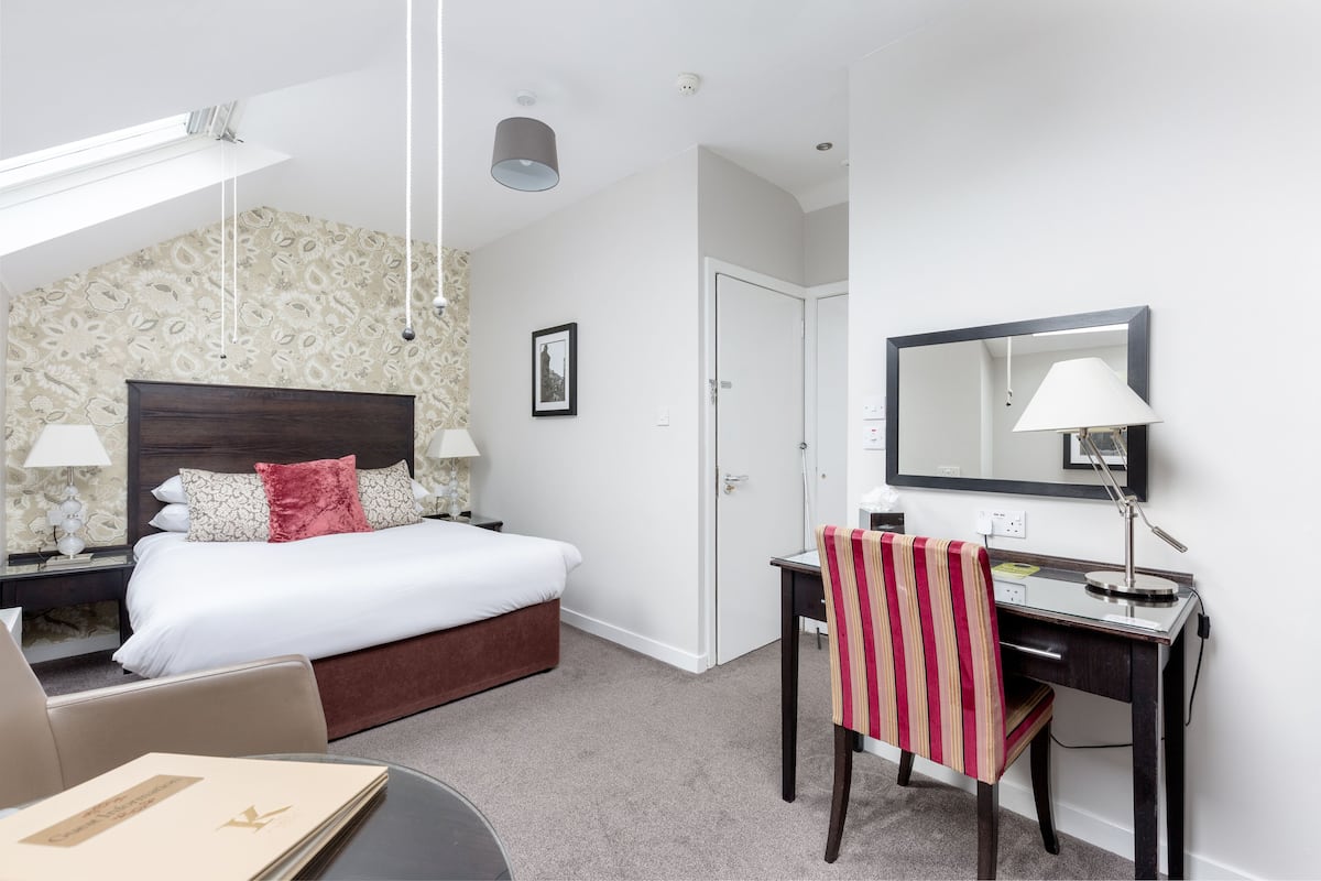 A hotel room with a bed, desk, chair, and a large mirror.