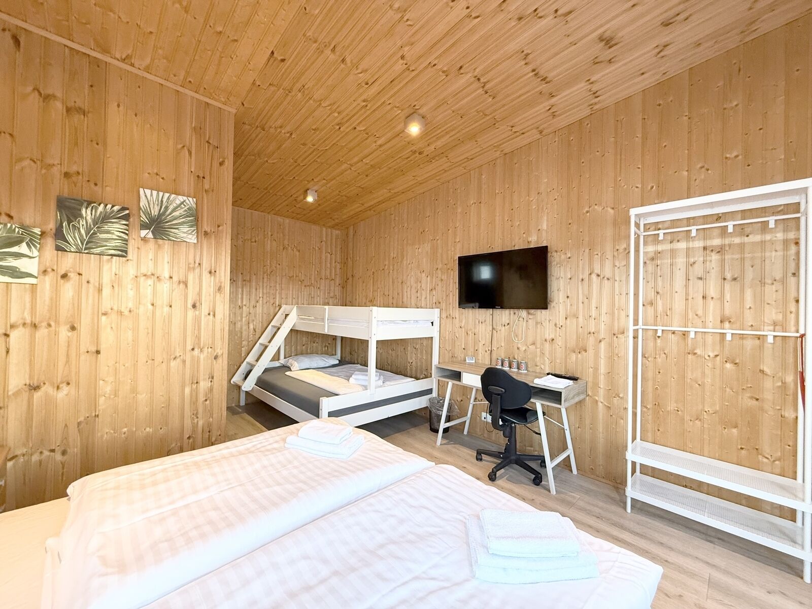 A wooden room with bunk beds, a desk, a chair, and a TV.