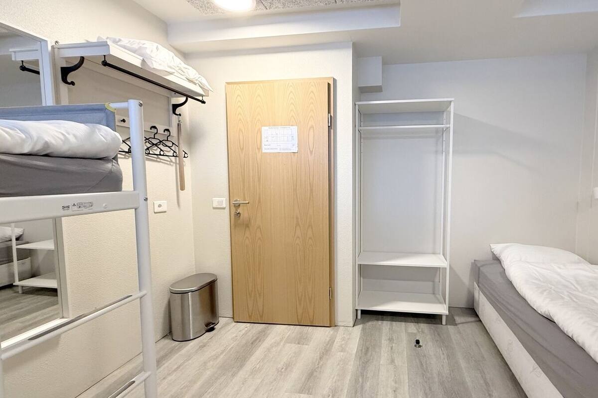 Ein Schlafraum mit Etagenbetten, einer Holztür, einem Kleiderschrank und einer kleinen Mülltonne.
