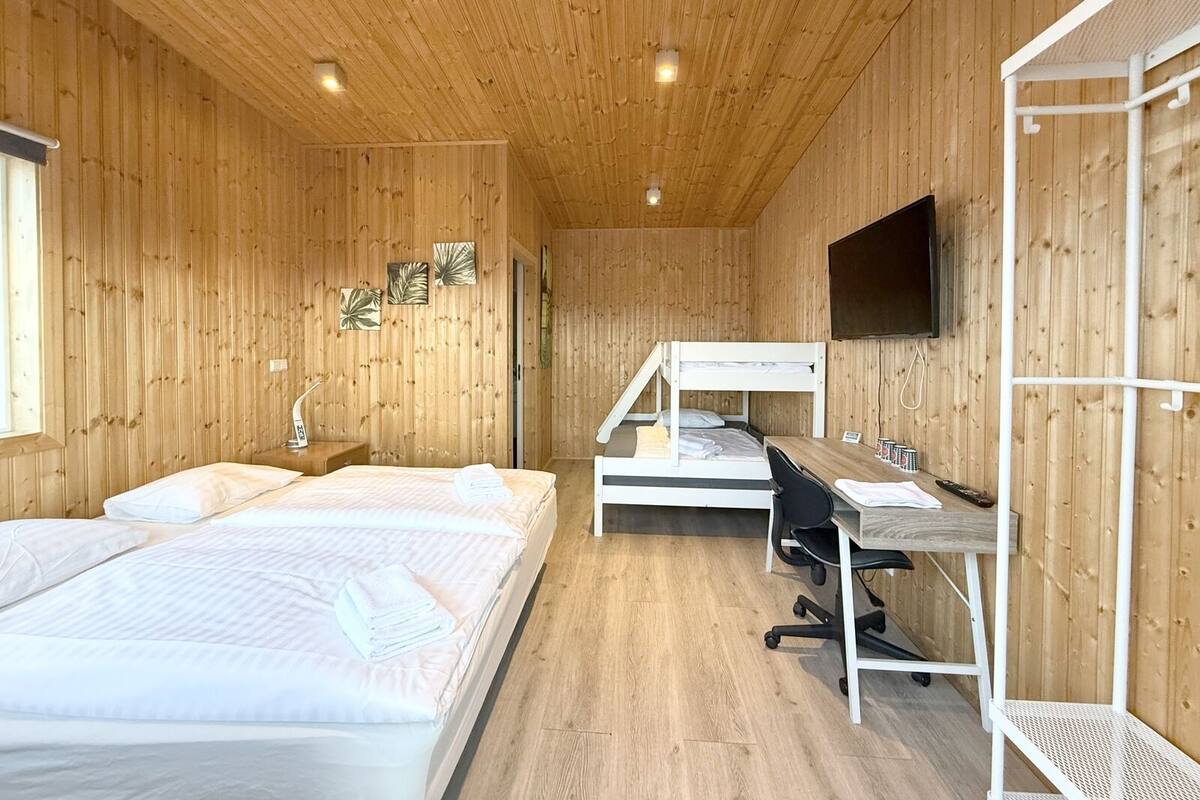 Ein Zimmer mit Holzwänden, zwei Betten, einem Schreibtisch, einem Stuhl und einem an der Wand befestigten Fernseher.