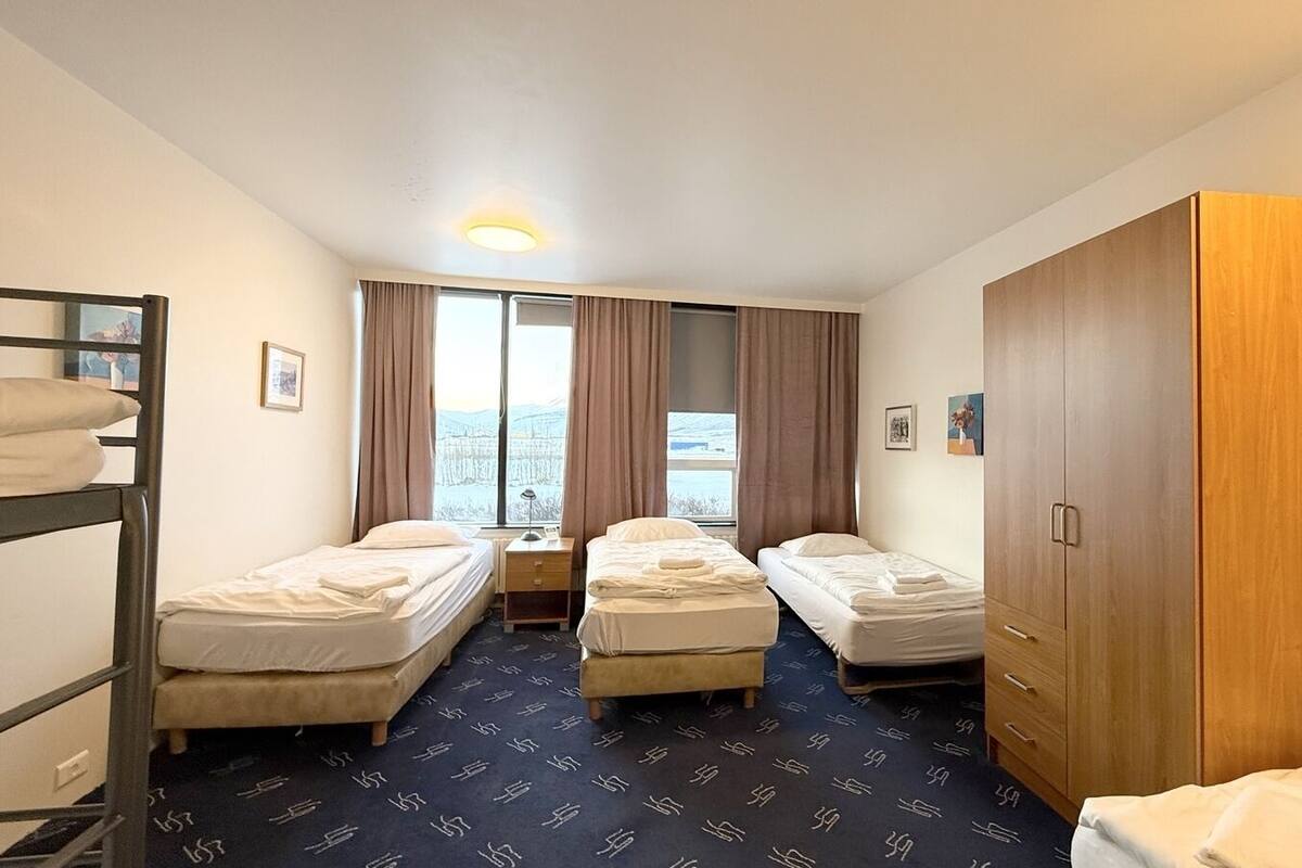 Ein Hotelzimmer mit zwei Einzelbetten, einem Etagenbett, einem Kleiderschrank und einem Fenster mit Vorhängen.