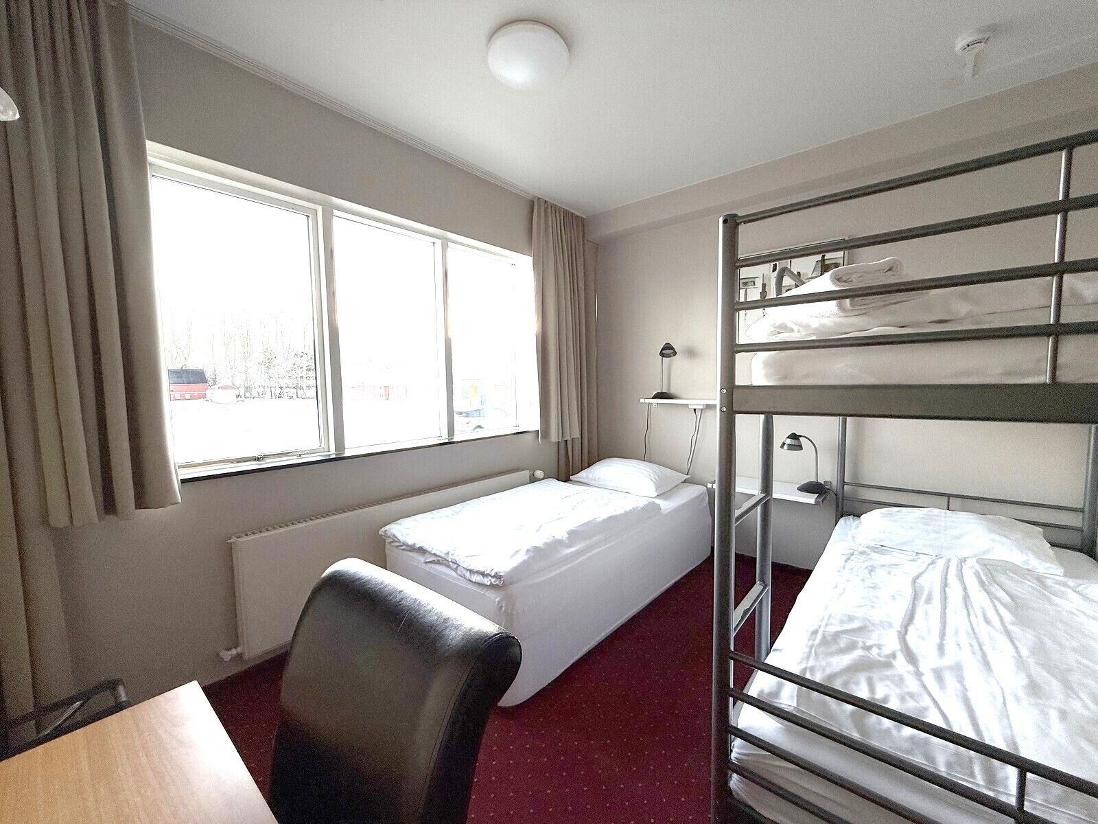 A hotel room with a bunk bed, a single bed, a desk, and a chair.