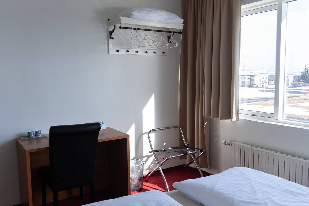 Ein Hotelzimmer mit Bett, Schreibtisch, Stuhl, Heizkörper und Fenster mit Blick ins Freie.
