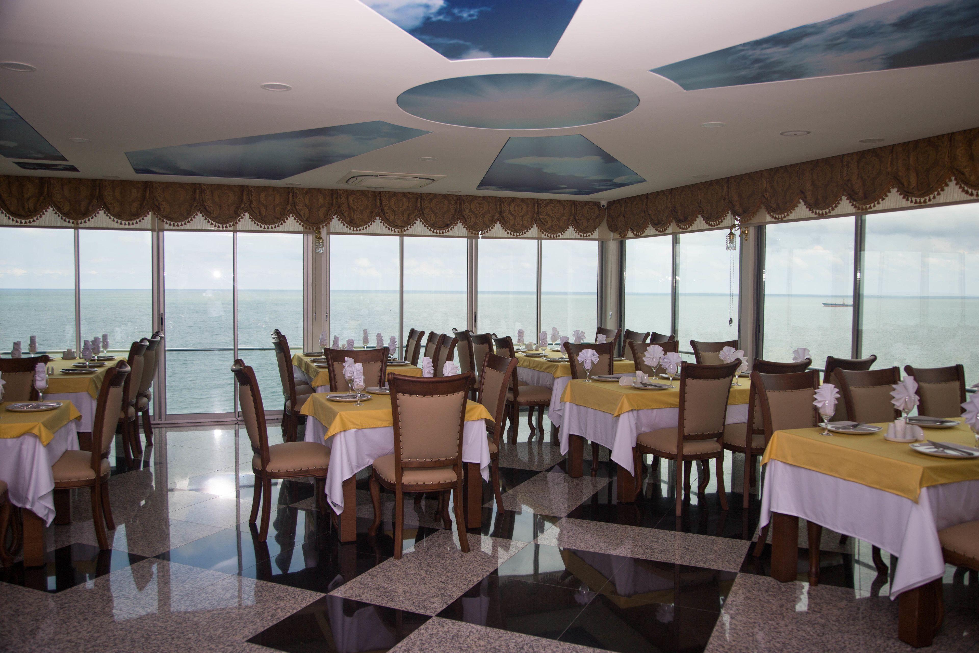 A restaurant with tables set for dining, large windows, and a view of the sea.