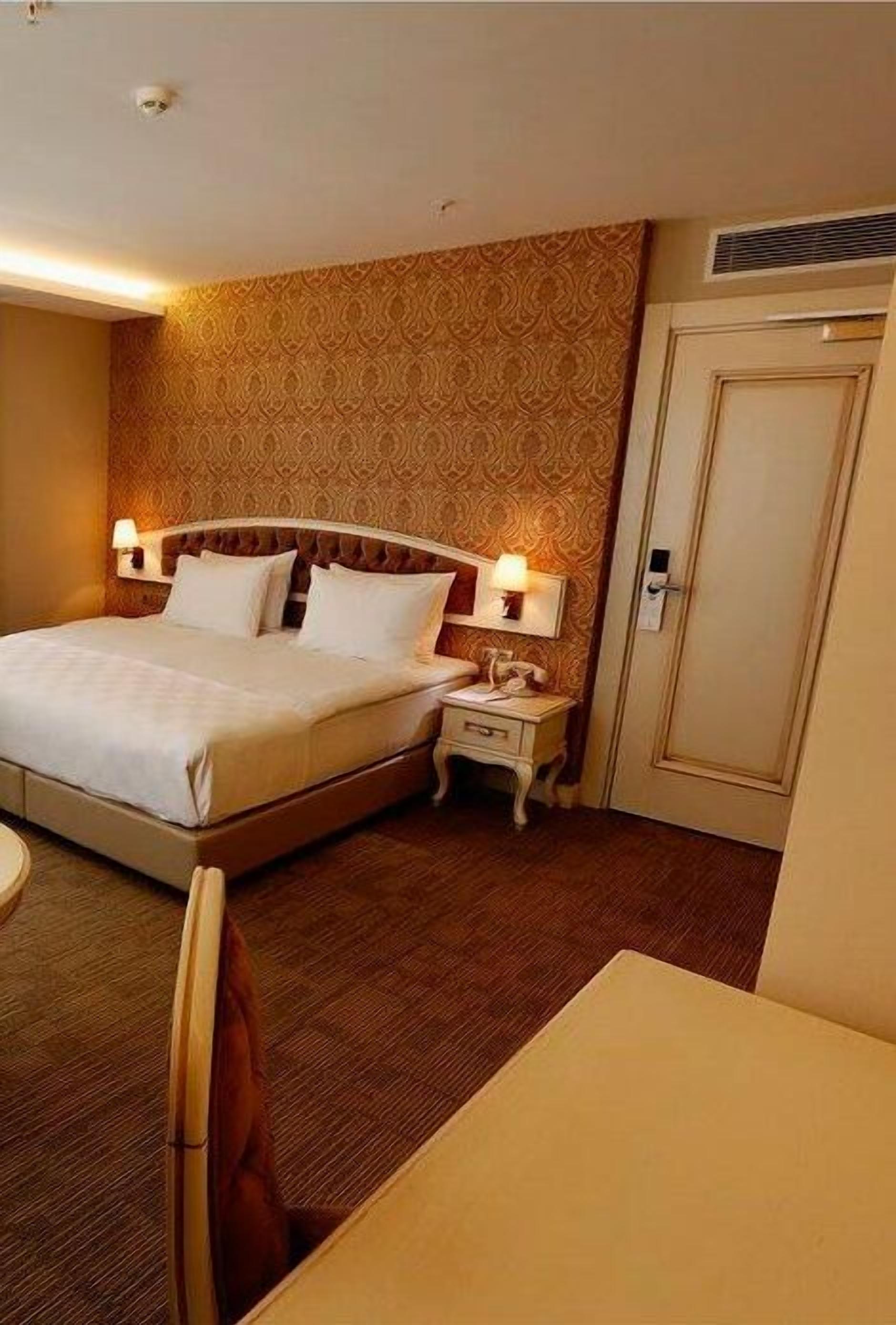 A hotel room with a large bed, bedside tables with lamps, a wardrobe, and a small round table.