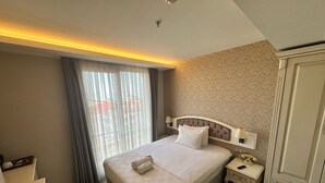 Une chambre d’hôtel avec un grand lit, une table de chevet, une commode et une fenêtre avec des rideaux.