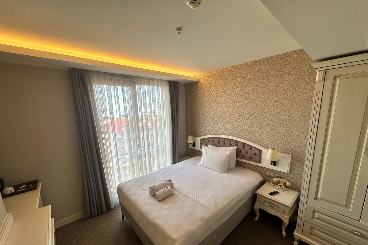 A hotel room with a large bed, a nightstand, a wardrobe, and a view through the window.