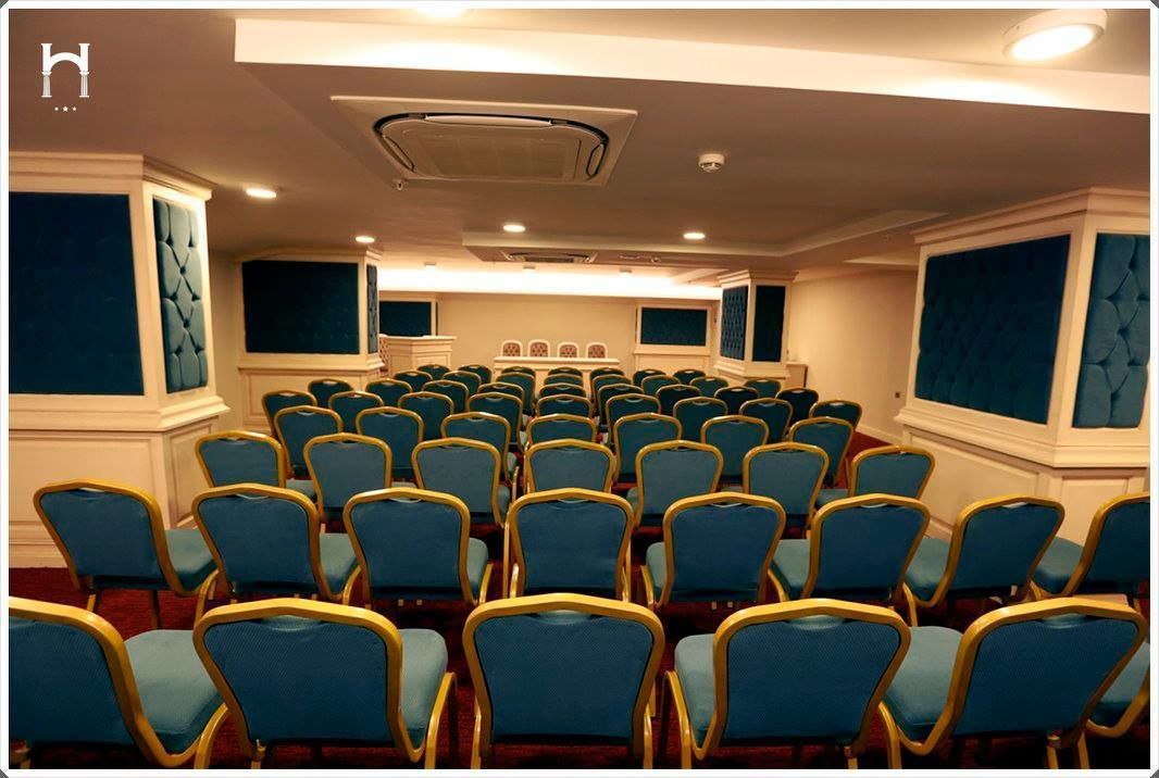 Un salón de conferencias con filas de sillas azules y un escenario al frente.