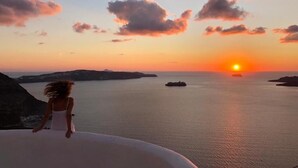 A sunset view from a coastal cliff with a person in a white dress overlooking the sea. - Villa Thiranthemis - Adults Only (Santorini)