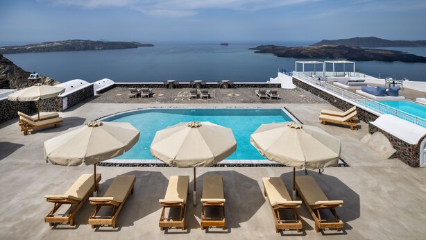 A pool area with lounge chairs and umbrellas, overlooking a calm sea and distant islands. - Villa Thiranthemis - Adults Only (Santorini)