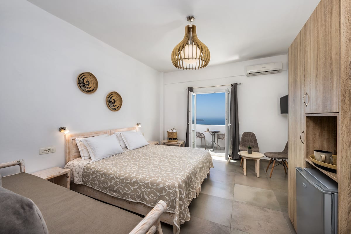 Une chambre à coucher comprenant un lit, des tables de chevet, une armoire en bois, une petite table avec des chaises et une vue à travers une porte vitrée.