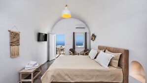 A bedroom with a large bed, a TV, a small table, and a view of the sea. - Villa Thiranthemis - Adults Only (Santorini)