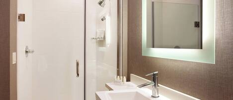 A modern bathroom with a glass-enclosed shower, a large mirror, and a white sink.