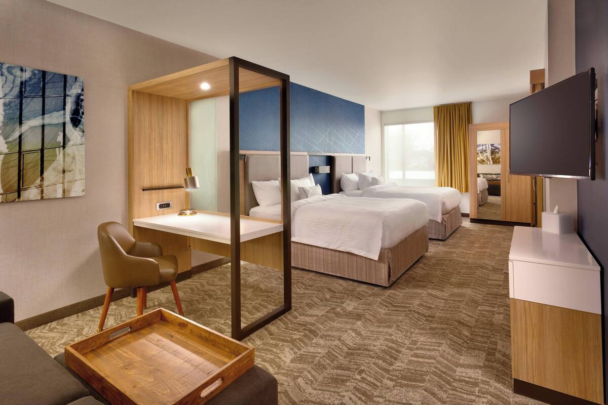 A hotel room with a desk, two beds, a TV, and a large window.
