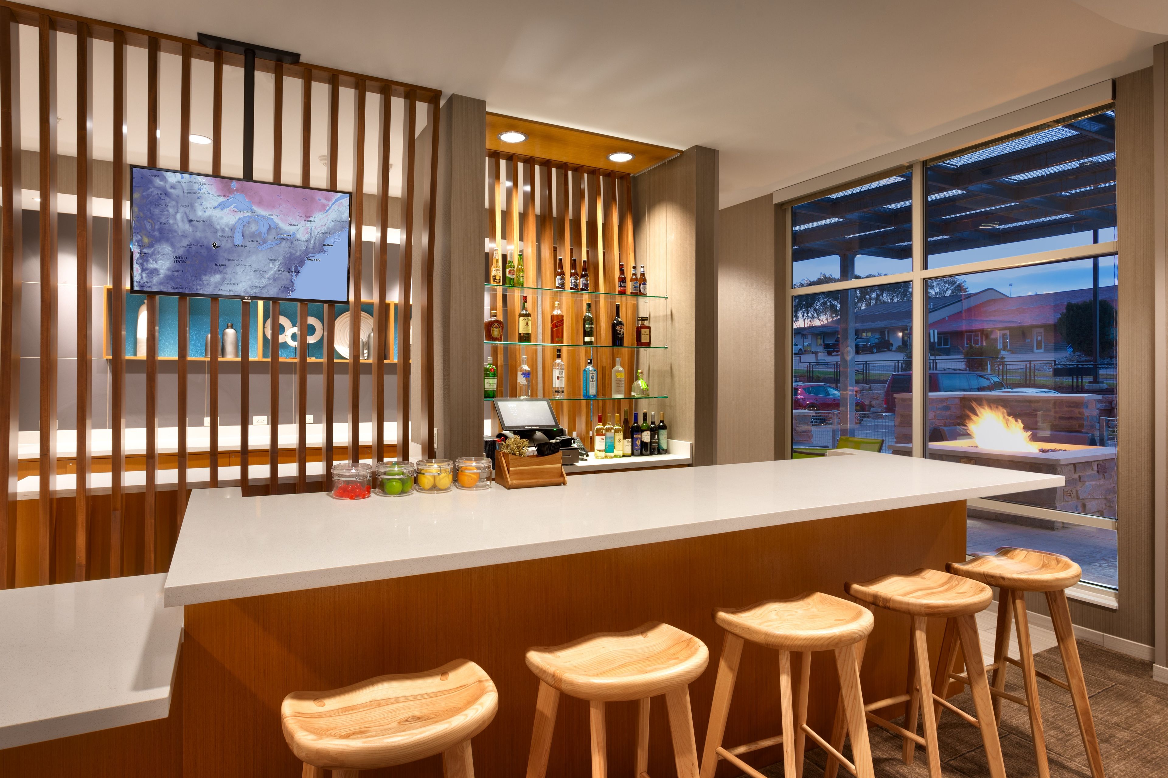 A bar area with a long counter, wooden stools, and a television screen displaying a map.