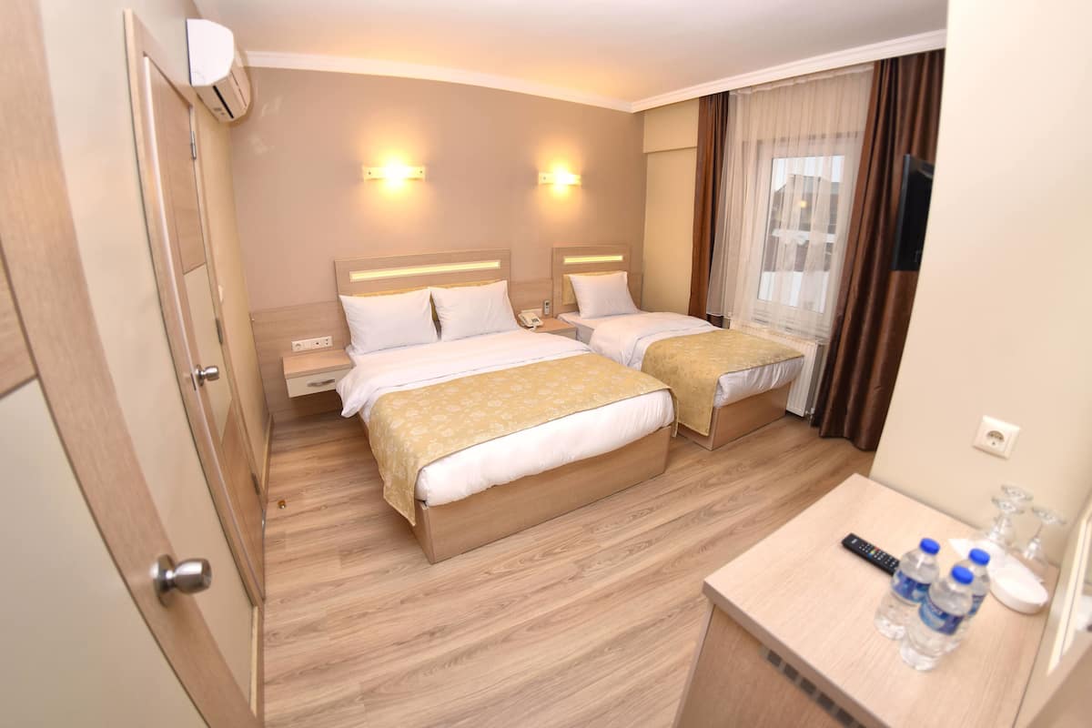 Habitación de hotel con dos camas, suelo de madera, una mesita de noche con control remoto y una pequeña mesa con botellas de agua.