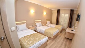 A hotel room with three single beds, a bedside table with a lamp, a small desk with a chair, and a TV mounted on the wall. - Sonerbey Otel (Ordu)