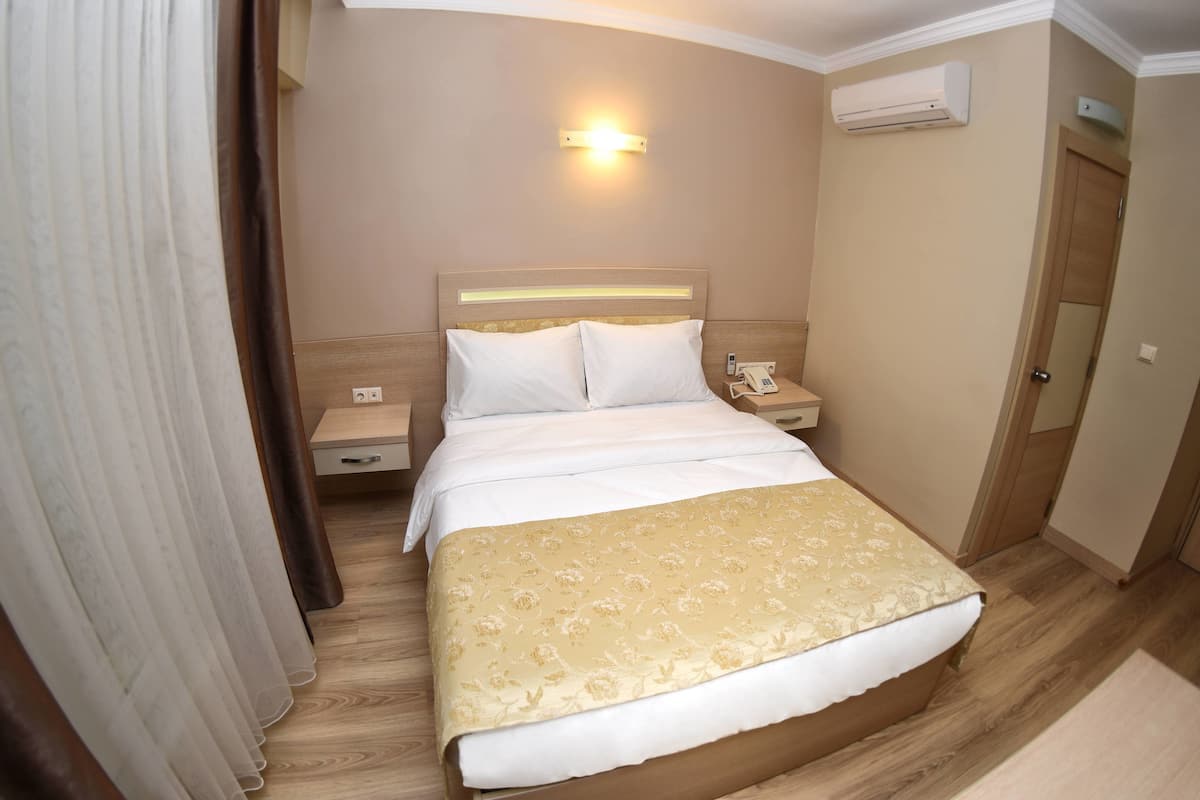 Una habitación de hotel con una cama, mesitas de noche, un teléfono y un equipo de aire acondicionado.