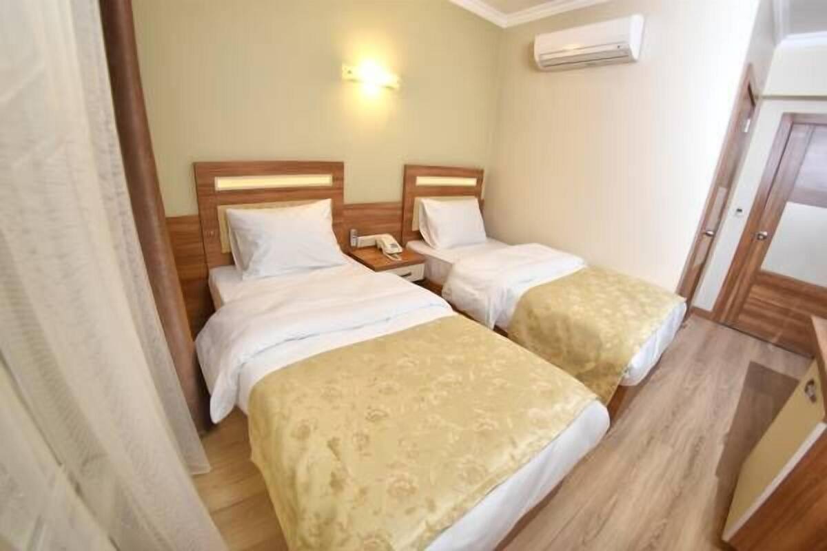 Una habitación de hotel con dos camas individuales, una mesita de noche con lámpara y un equipo de aire acondicionado en la pared.