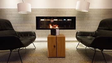 Una sala moderna con dos sillones de cuero, una mesa de centro de madera, un televisor de pantalla plana y una chimenea con fuego a la vista.