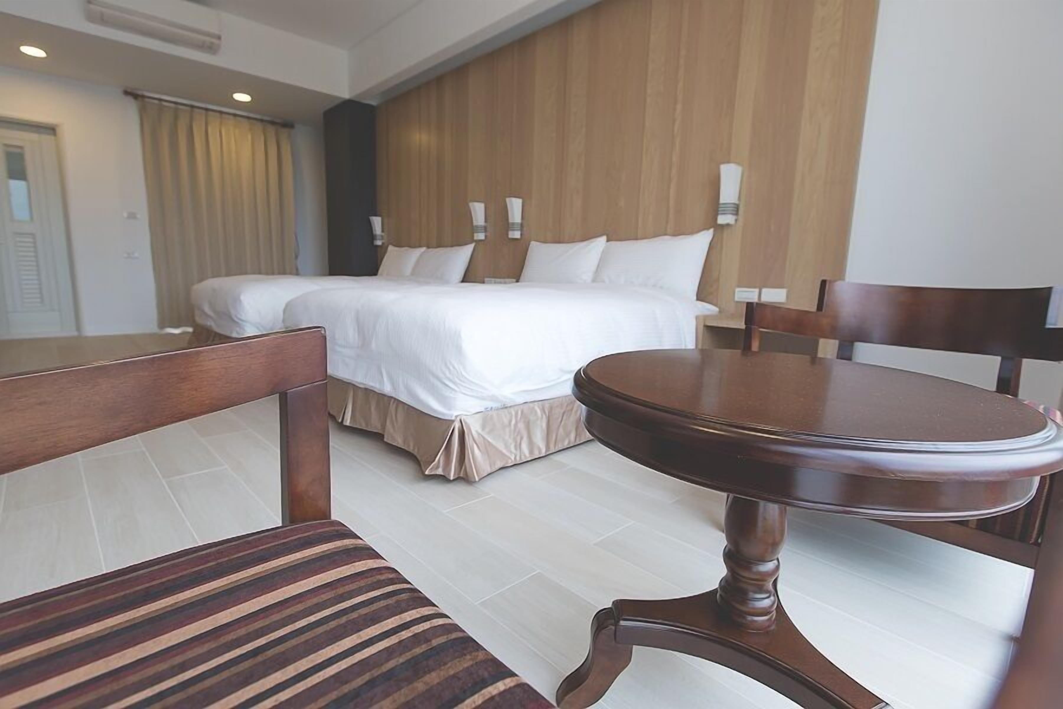 Een hotelkamer met een groot bed, een houten hoofdbord, een ronde tafel en een gestreept stoeltje.