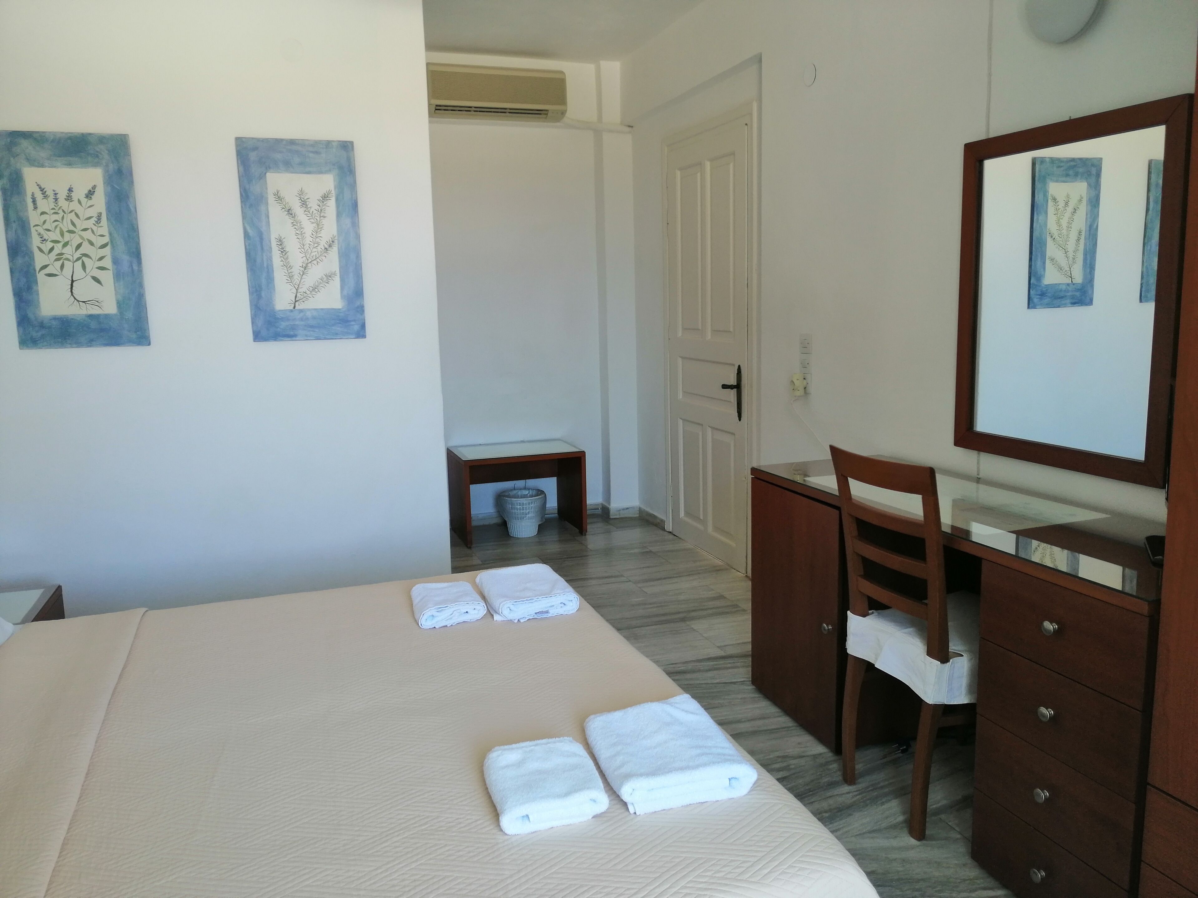 A hotel room with a bed, a wooden dresser with a mirror, and two wall-mounted artwork pieces.