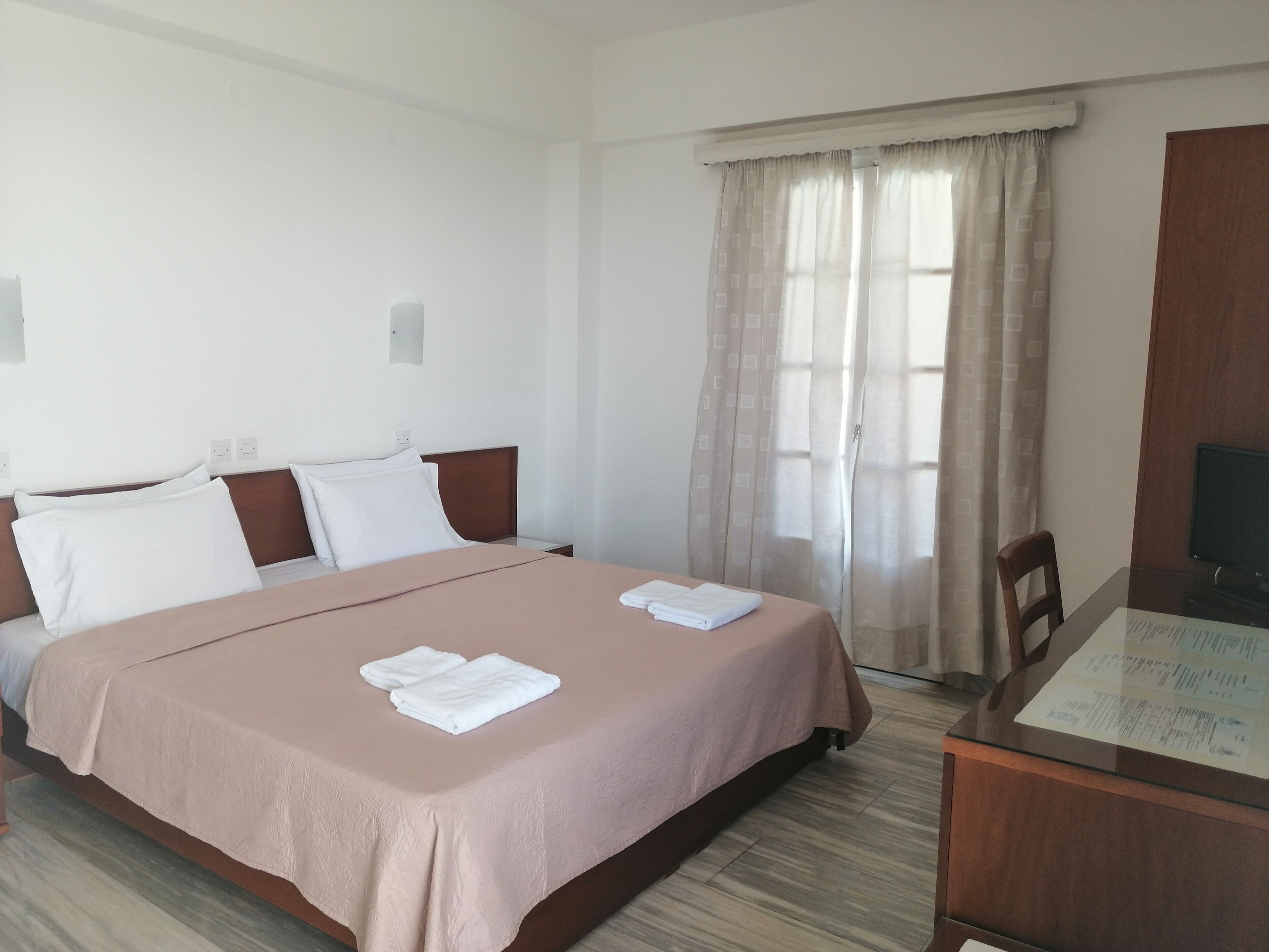 A hotel room with a large bed, a desk with a chair, and a window with curtains.