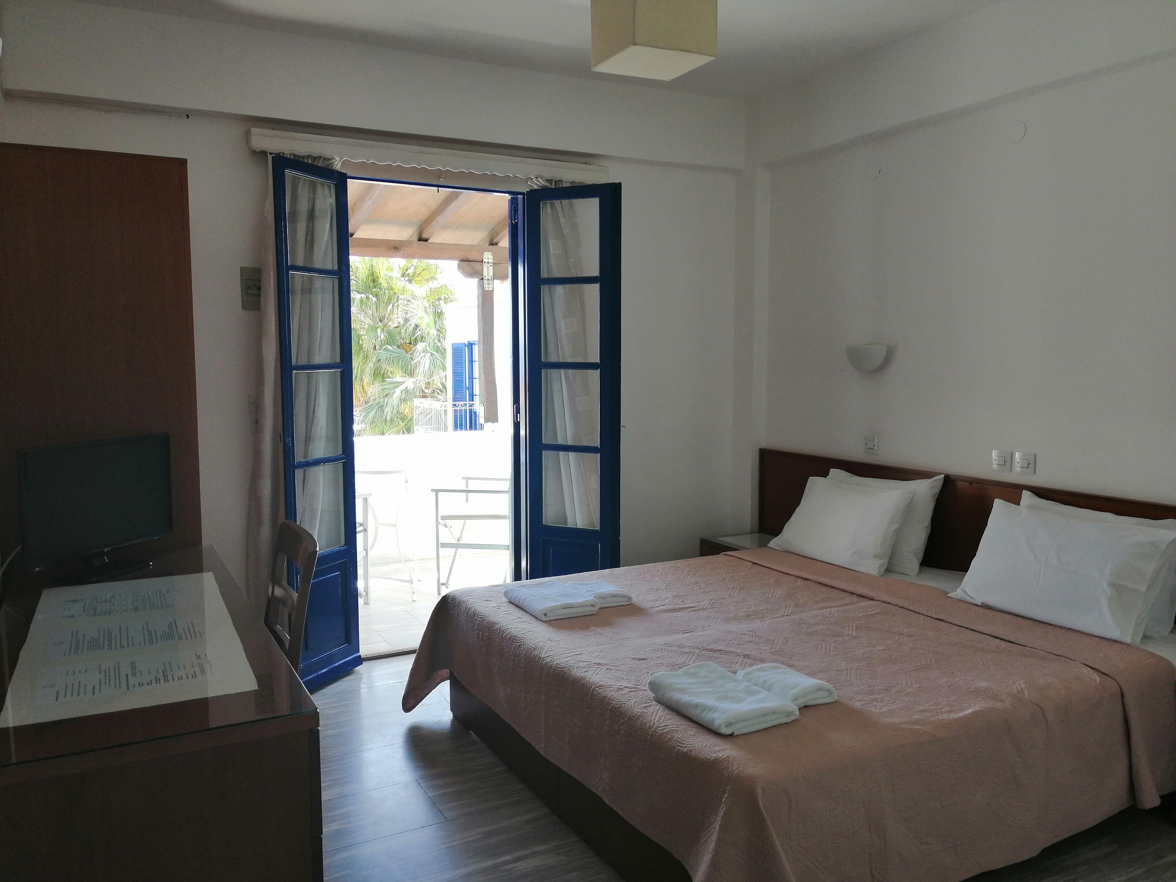 Une chambre d’hôtel avec un lit, une télévision, un bureau et une vue sur l’extérieur, grâce à une porte ouverte.