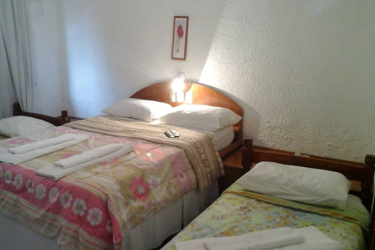 Habitación de hotel con dos camas, cada una con una colcha de motivos florales y almohadas blancas. Hay un cuadro en la pared y una mesita de noche con una lámpara.