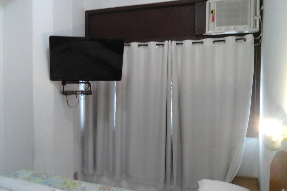Una habitación con cama, televisión montada en la pared y cortina.
