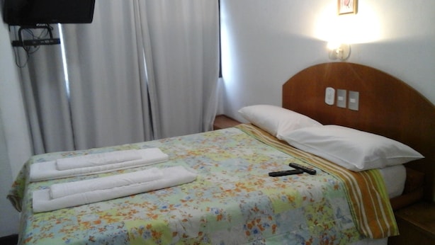 A hotel room with a bed, a TV mounted on the wall, and a window with curtains. - Center Hotel Barra (Rio de Janeiro)