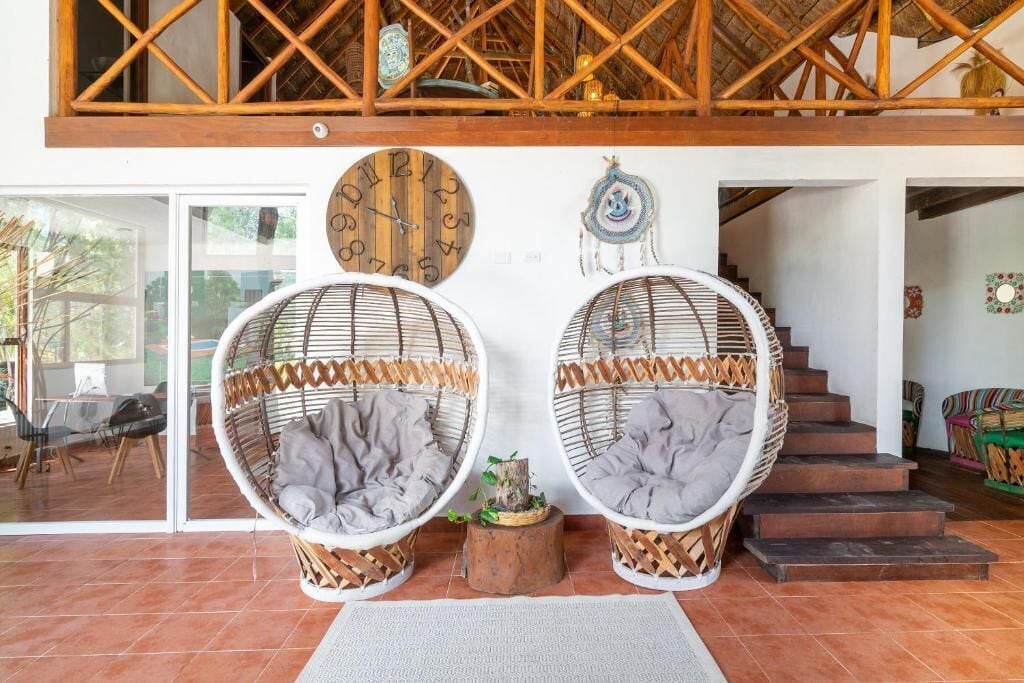 Una habitación con dos sillones de mimbre, una escalera de madera y un reloj de pared.