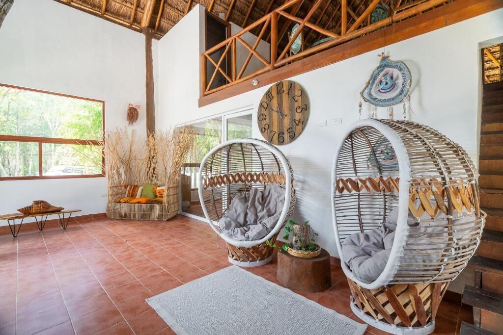Una habitación con dos sillones colgantes de mimbre, un banco de madera y un ventanal grande.