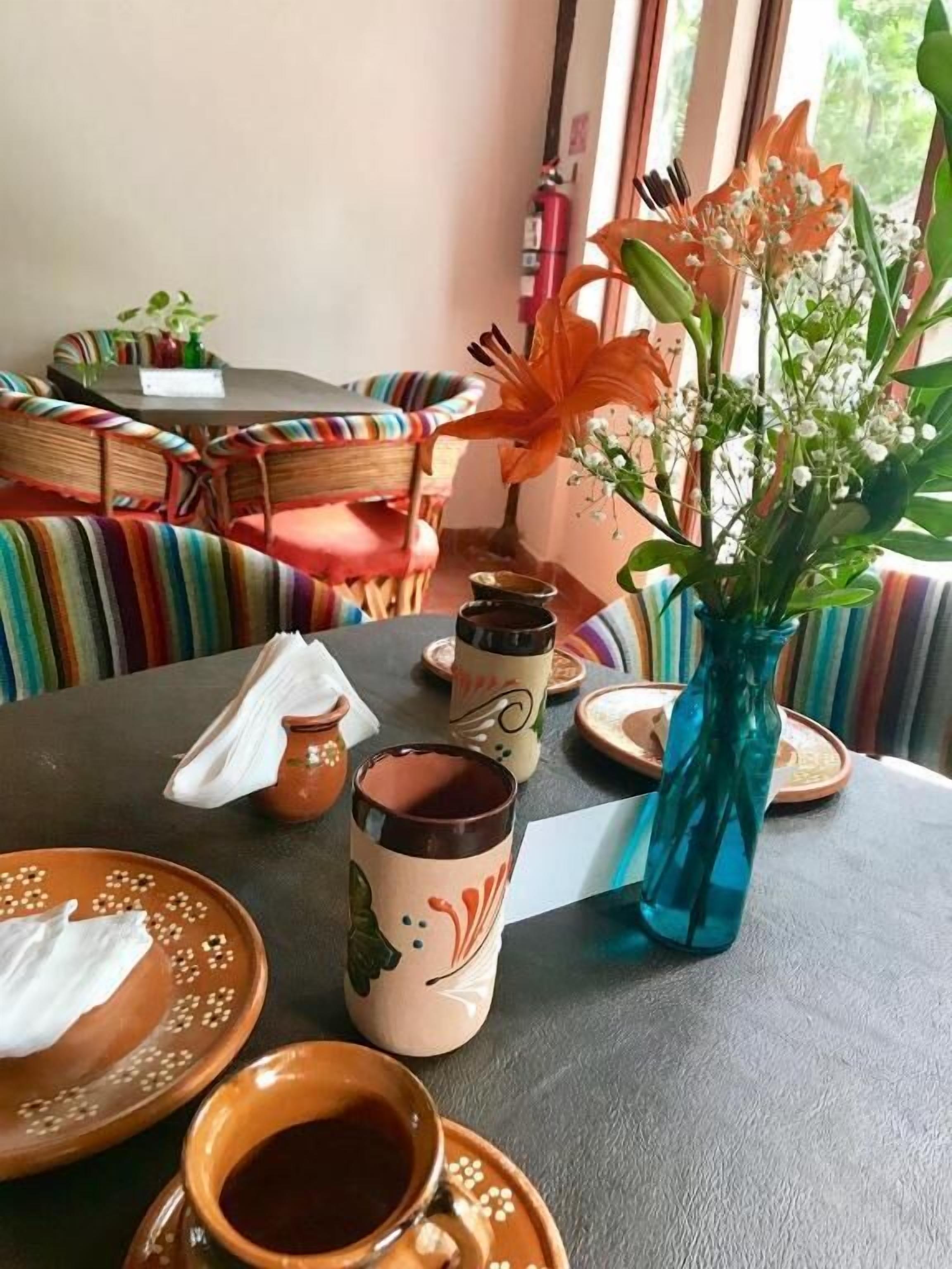 A dining area with a table set for two, featuring a vase with flowers, a teapot, and a cup.